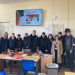Students and staff in a classroom beside a screen showing ALONE's Christmas Jumper Day 2024 poster