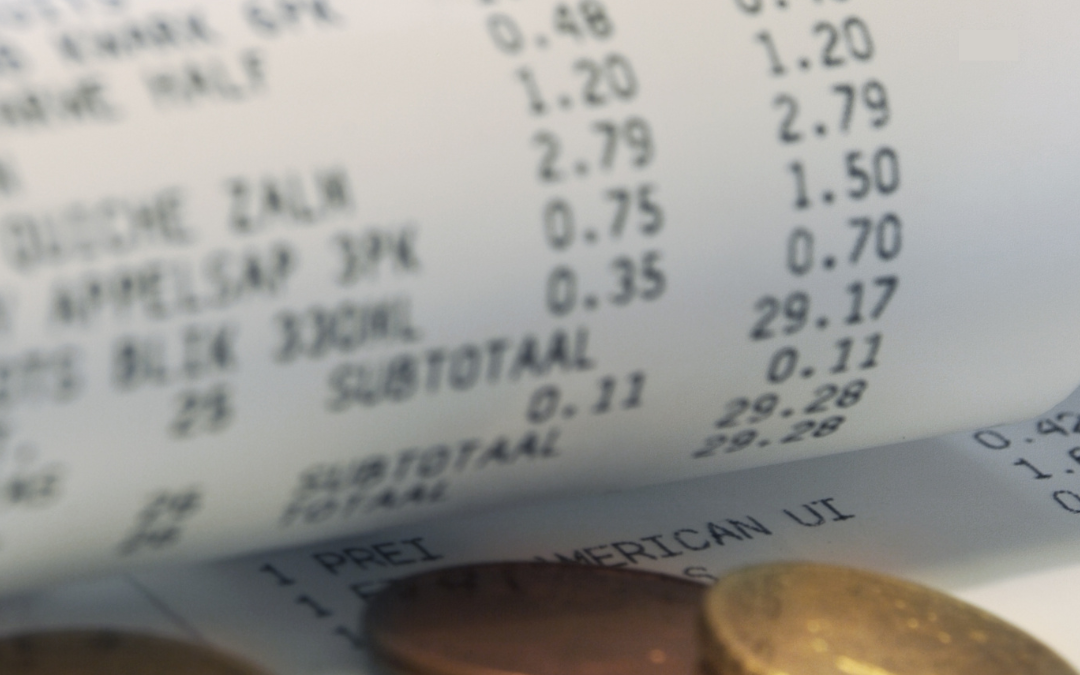 Close-up of a curled shopping receipt showing grocery prices with a few small coins beside it