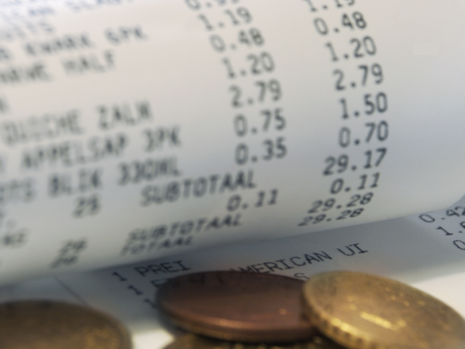 Close-up of a curled shopping receipt showing grocery prices with a few small coins beside it