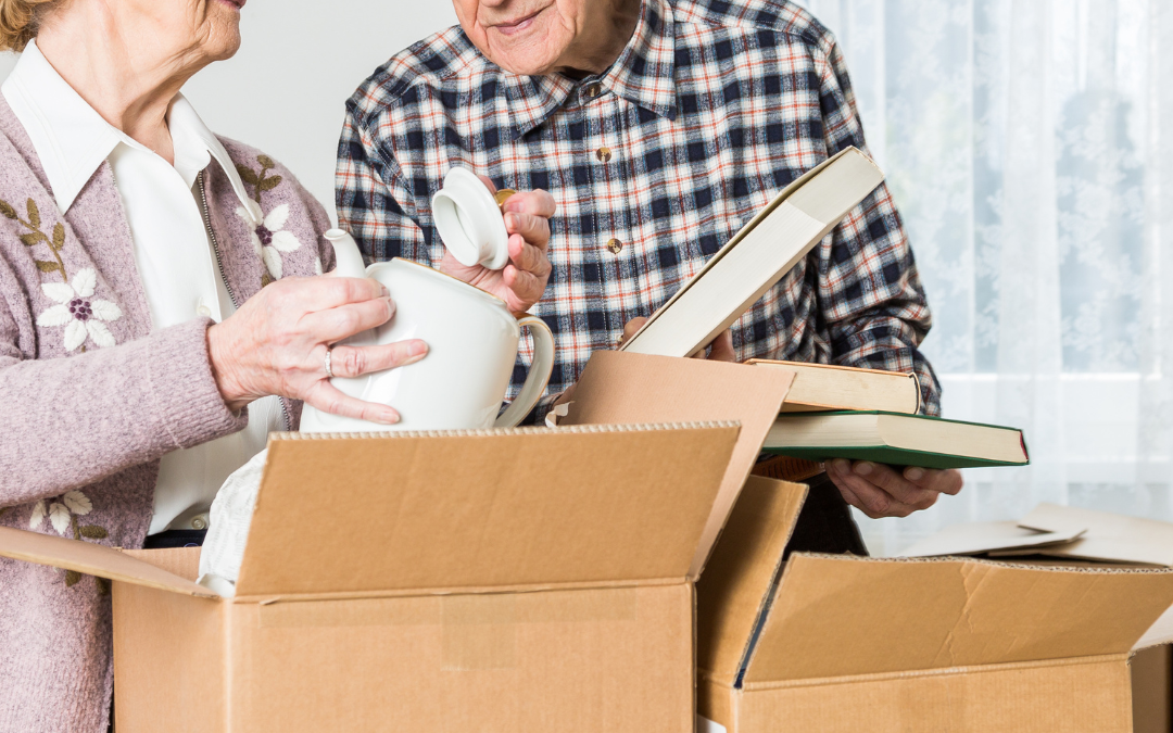 Older couple packing china and books into cardboard boxes as they prepare to move home