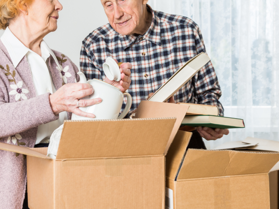 Older couple packing china and books into cardboard boxes as they prepare to move home