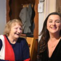 An older woman and a younger woman laughing together in a home sitting room