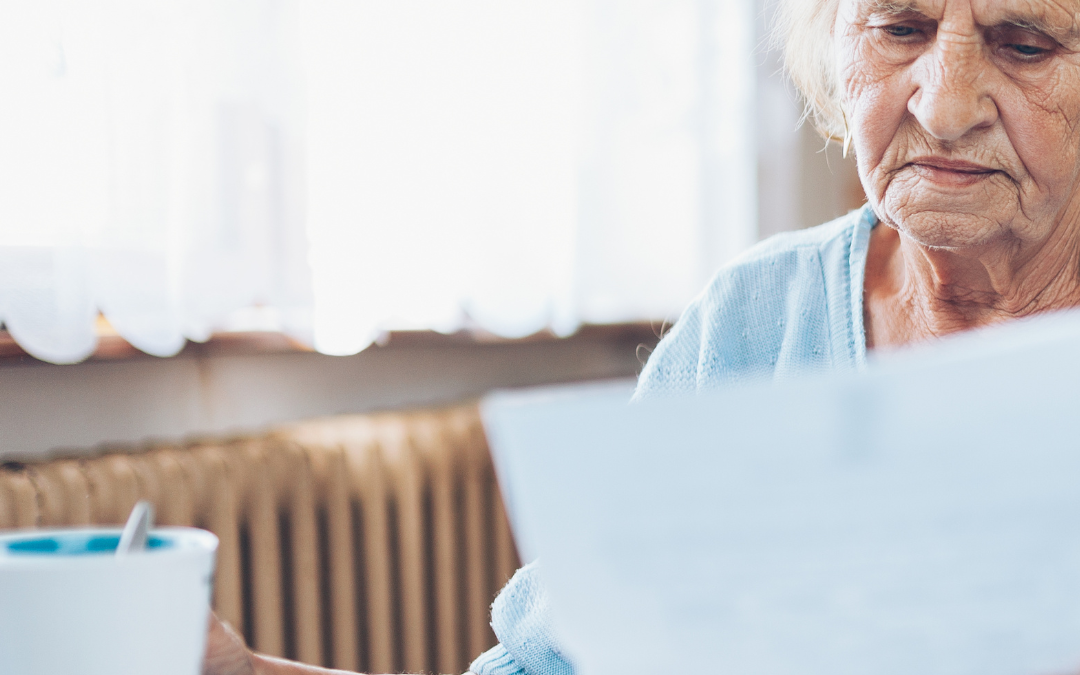 Older woman at a table with a cup of tea, reading paperwork with a concerned expression