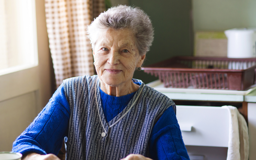 Older woman sitting at her kitchen table at home, smiling, with glasses and a cup in front of her