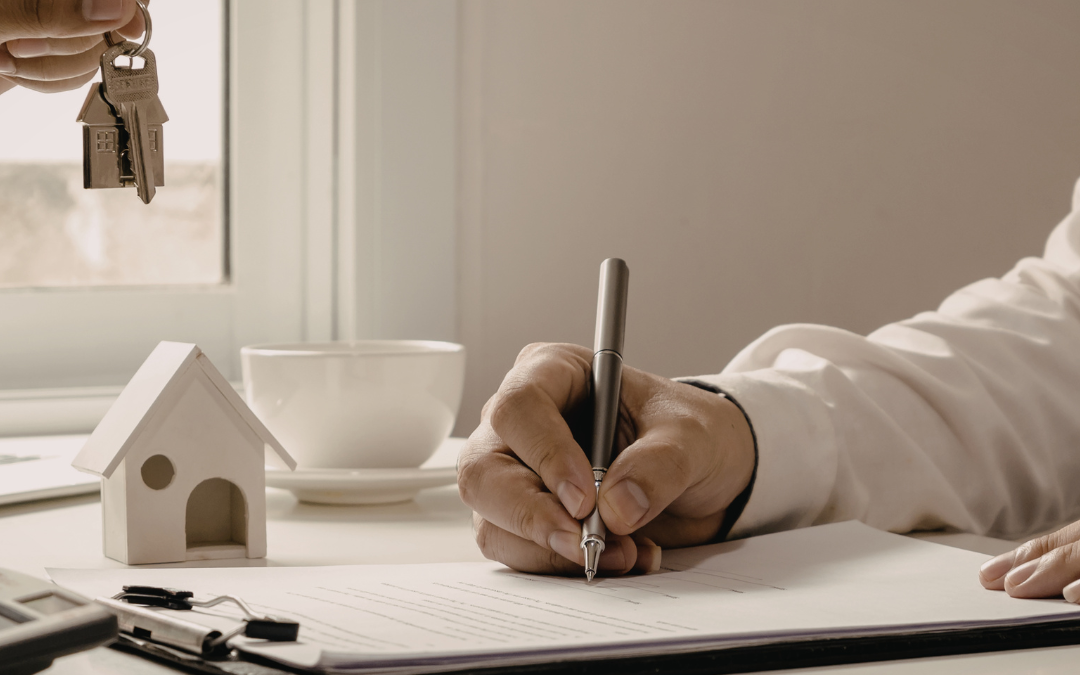 A person signing housing paperwork at a desk while another hand holds out house keys