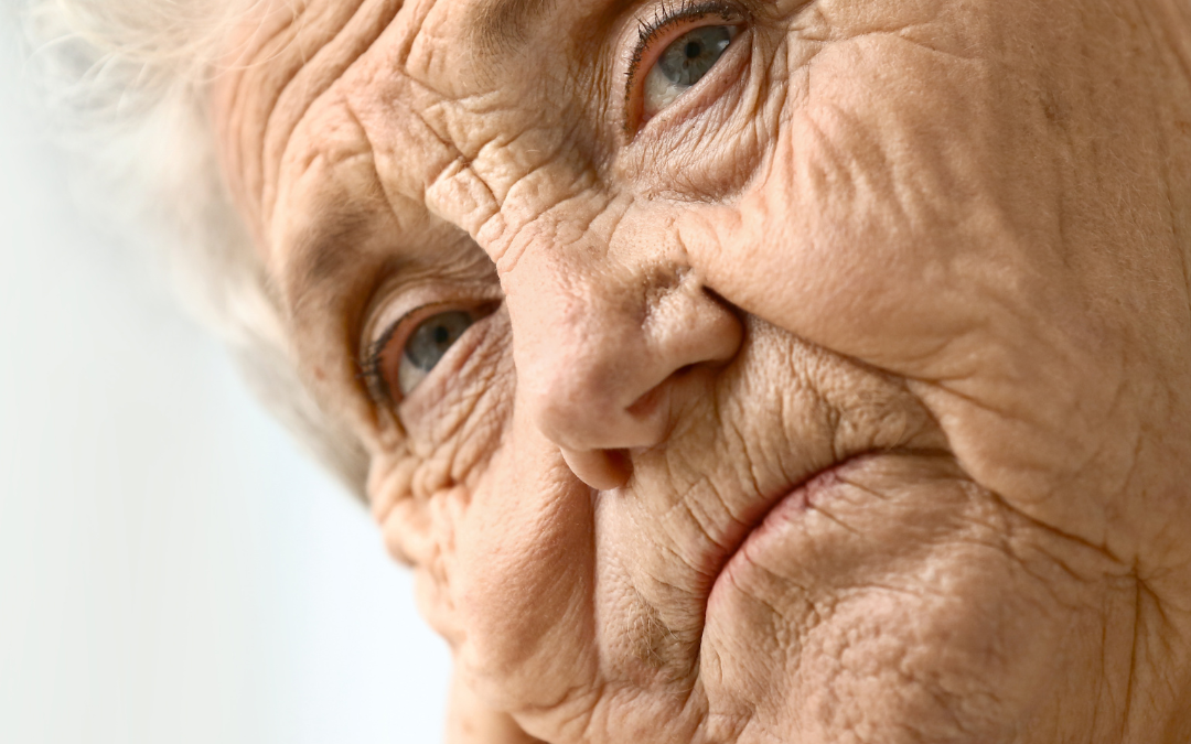 Close-up of an older woman with white hair resting her chin on her hand, looking thoughtfully into the distance