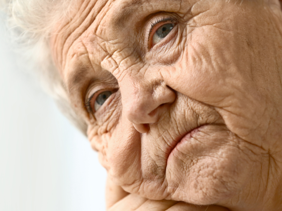 Close-up of an older woman with white hair resting her chin on her hand, looking thoughtfully into the distance