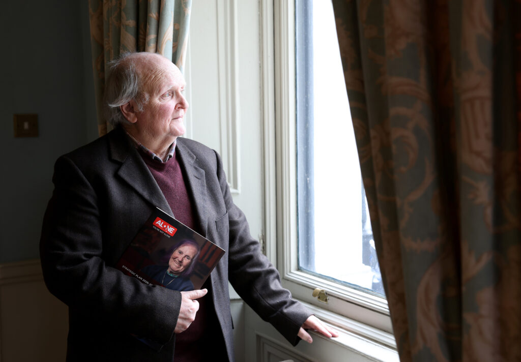 An older man in a jacket holds ALONE's Strategic Plan booklet while looking out a window