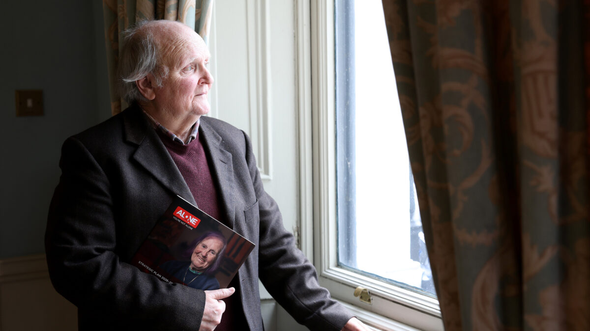 An older man in a jacket holds ALONE's Strategic Plan booklet while looking out a window