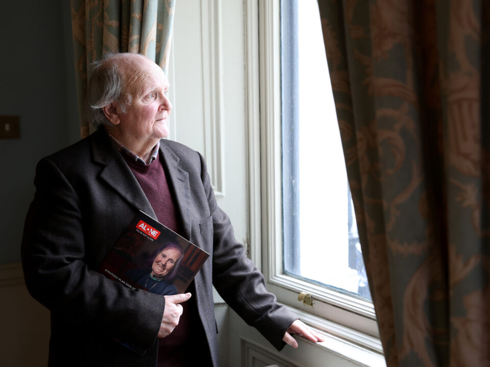 An older man in a jacket holds ALONE's Strategic Plan booklet while looking out a window