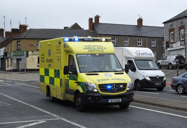 National Ambulance Service ambulance with blue lights flashing driving through an Irish town street