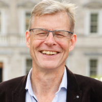 Seán Moynihan Seán Moynihan smiling, wearing glasses, a light blue shirt and dark jacket, outside a Georgian building