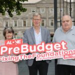 Three people outside Leinster House holding an ALONE sign reading '#PreBudget FixingTheFoundations Pre-budget2027'