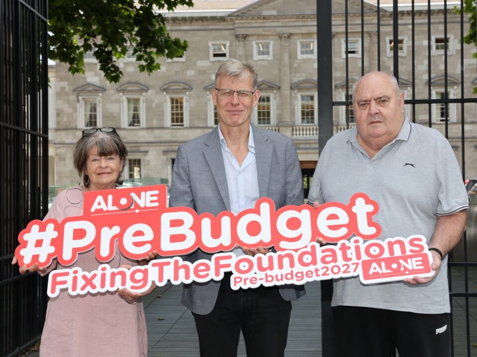 Three people outside Leinster House holding an ALONE sign reading '#PreBudget FixingTheFoundations Pre-budget2027'