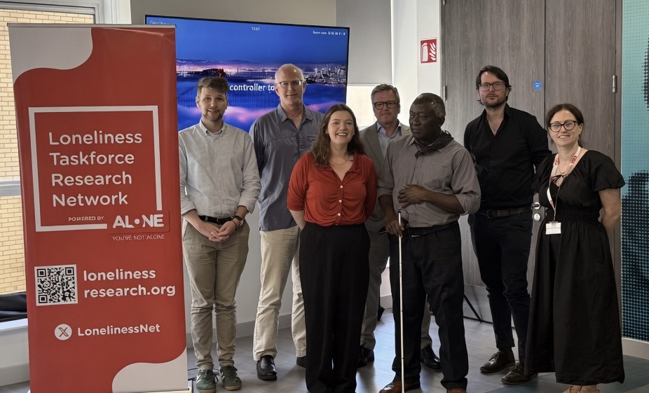 Group of seven people standing beside a Loneliness Taskforce Research Network banner at an ALONE event