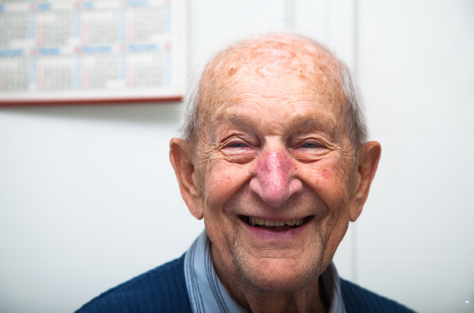 An older man smiling warmly at home, with a wall calendar behind him