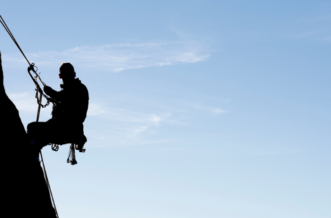 Silhouette of an abseiler on ropes against a clear blue sky